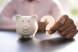 Piggy bank with man holding question mark next to it.